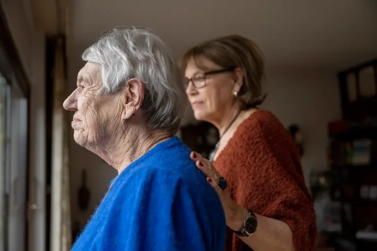 two elderly friends standing looking out window