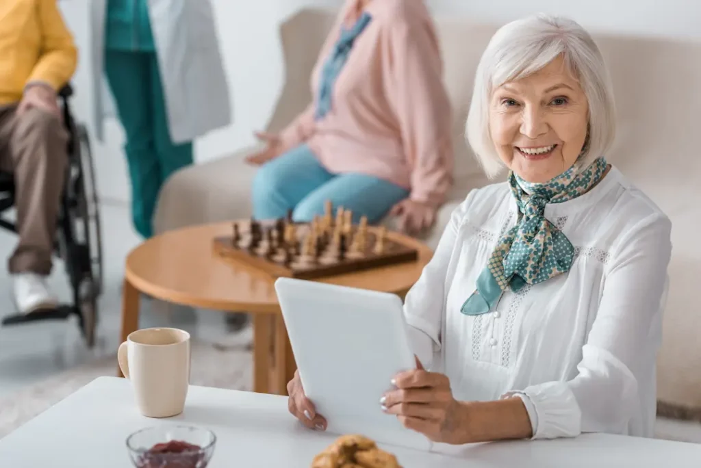 senior woman using digital tablet at nursing home with blurred people at background